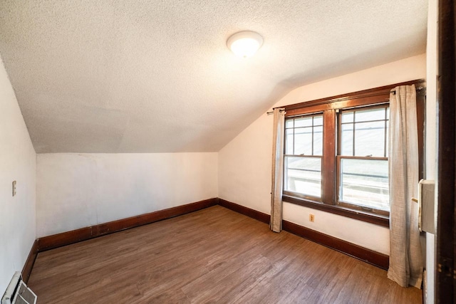 additional living space with baseboard heating, hardwood / wood-style floors, vaulted ceiling, and a textured ceiling