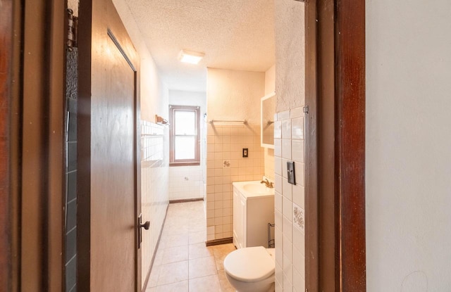 bathroom featuring toilet, tile patterned flooring, vanity, tile walls, and a textured ceiling