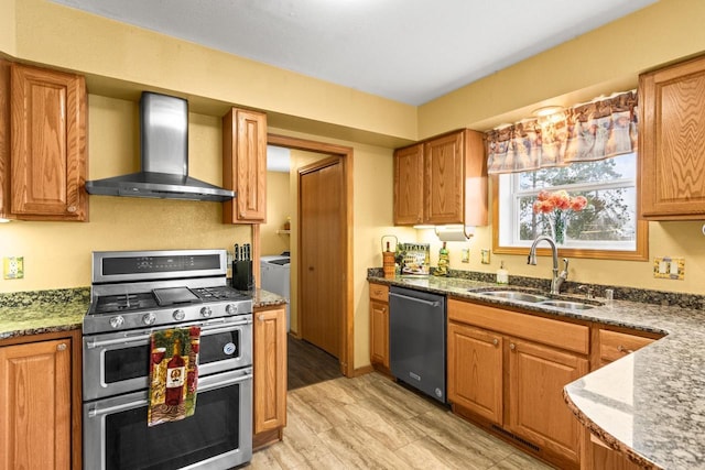 kitchen with appliances with stainless steel finishes, light wood-type flooring, sink, wall chimney range hood, and dark stone countertops