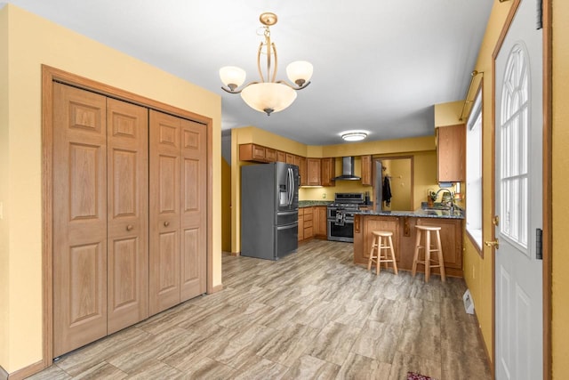 kitchen featuring wall chimney exhaust hood, stainless steel appliances, kitchen peninsula, pendant lighting, and a kitchen bar