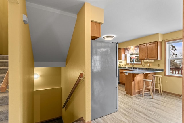 kitchen with plenty of natural light, a kitchen bar, stainless steel refrigerator, and light hardwood / wood-style flooring