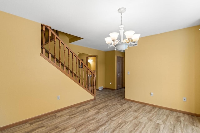 empty room with light wood-type flooring and a chandelier