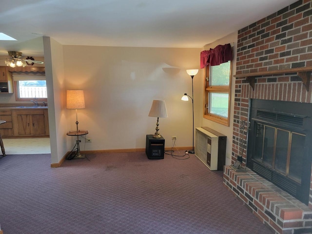 unfurnished living room with sink, dark colored carpet, a brick fireplace, and ceiling fan