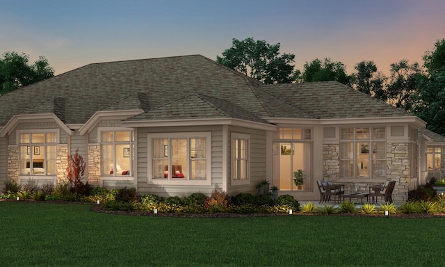 view of front of home featuring stone siding, roof with shingles, and a lawn