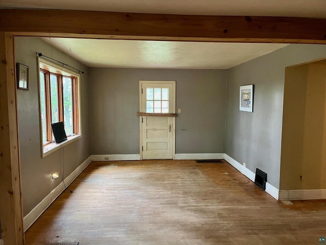 spare room with beamed ceiling and light wood-type flooring