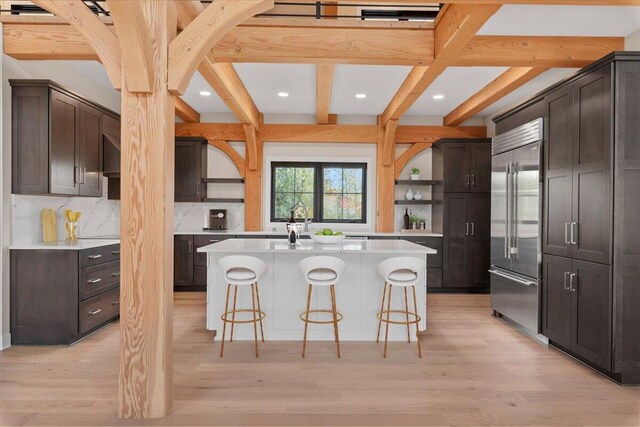 kitchen featuring light wood-style flooring, a kitchen breakfast bar, open shelves, beam ceiling, and built in fridge