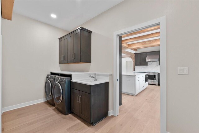 washroom featuring cabinet space, light wood-style floors, a sink, and washing machine and clothes dryer