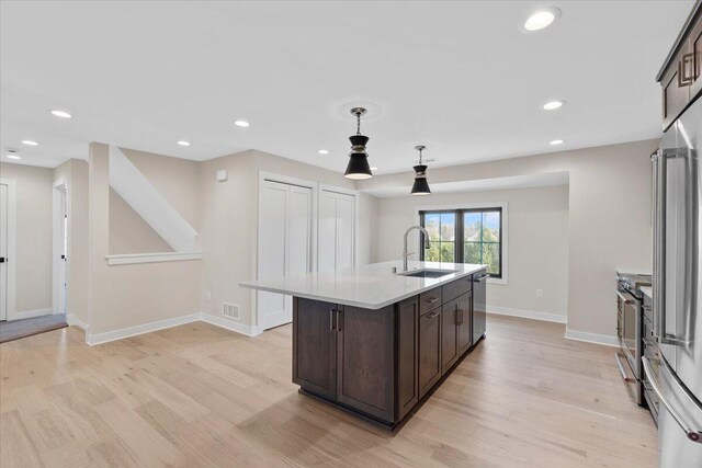 kitchen featuring stainless steel appliances, a sink, dark brown cabinets, light countertops, and light wood-type flooring