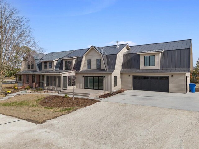 view of front facade with driveway, a garage, a gambrel roof, metal roof, and a standing seam roof