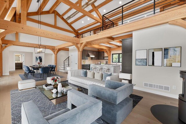 living area featuring high vaulted ceiling, wood finished floors, visible vents, baseboards, and stairway