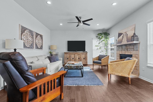 living room with dark wood-type flooring, a stone fireplace, and ceiling fan