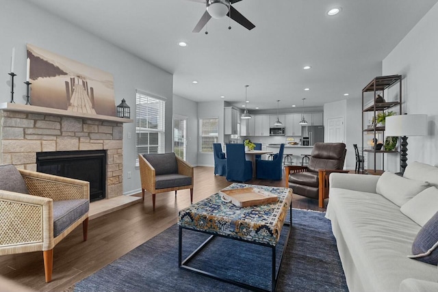 living room with dark wood-type flooring, ceiling fan, and a stone fireplace