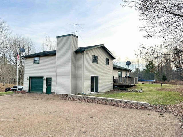 back of house featuring a garage, a yard, a trampoline, and a wooden deck