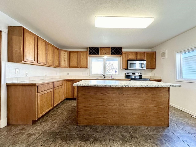 kitchen with appliances with stainless steel finishes, a textured ceiling, a center island, and sink