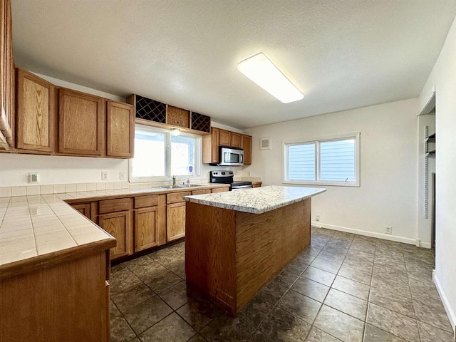 kitchen with a kitchen island, appliances with stainless steel finishes, a textured ceiling, dark tile patterned floors, and sink