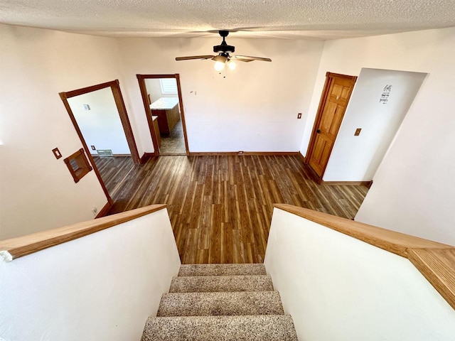 stairway with a textured ceiling, hardwood / wood-style flooring, and ceiling fan