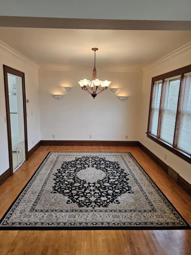 unfurnished dining area featuring crown molding, a notable chandelier, and hardwood / wood-style flooring