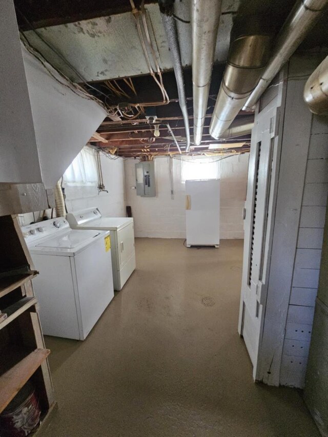 basement featuring washing machine and dryer, electric panel, and white refrigerator