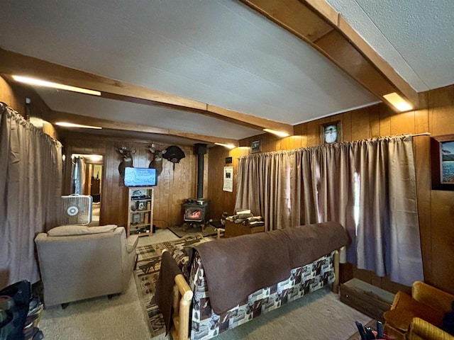 carpeted cinema room featuring a wood stove, wood walls, and beamed ceiling