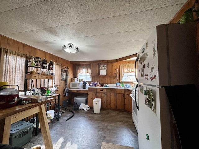 kitchen featuring a textured ceiling, white appliances, dark wood-type flooring, and wooden walls