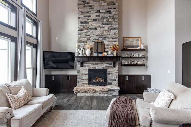 living room with a stone fireplace, dark wood-type flooring, and a towering ceiling