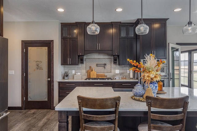 kitchen with dark wood-type flooring, light stone counters, hanging light fixtures, a breakfast bar area, and dark brown cabinets