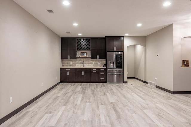 kitchen with dark brown cabinets, stainless steel fridge with ice dispenser, light wood-type flooring, and decorative backsplash