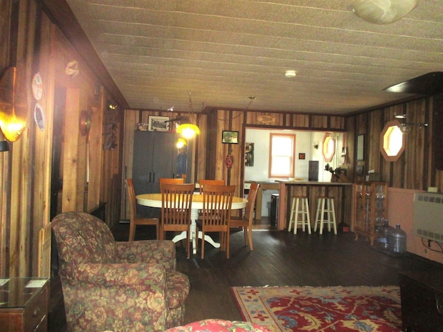 dining space featuring dark wood-type flooring, heating unit, and wooden walls