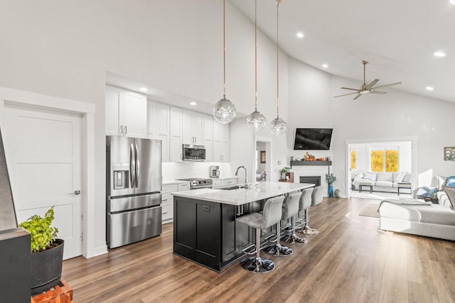 kitchen with an island with sink, hanging light fixtures, sink, white cabinets, and appliances with stainless steel finishes