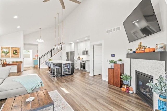 living room featuring ceiling fan, high vaulted ceiling, light hardwood / wood-style flooring, and a fireplace