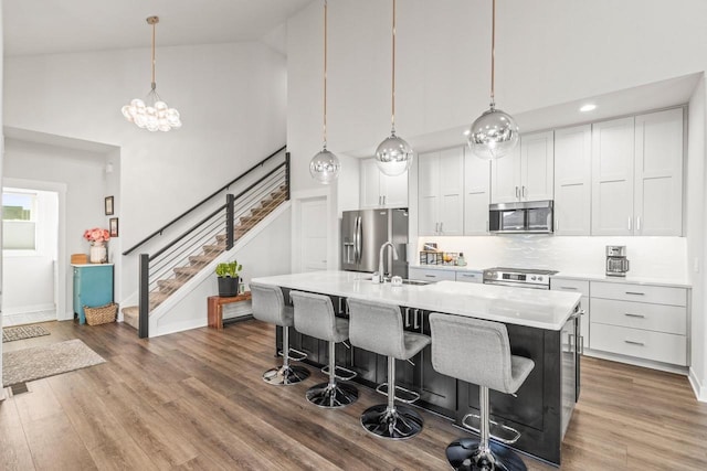 kitchen featuring hardwood / wood-style floors, a center island with sink, high vaulted ceiling, stainless steel appliances, and sink