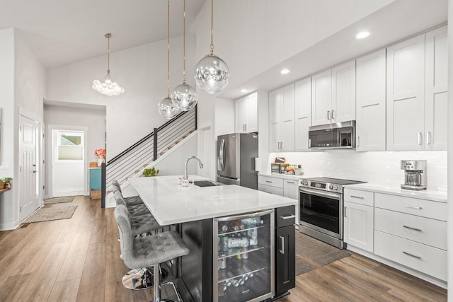 kitchen featuring a center island with sink, appliances with stainless steel finishes, decorative light fixtures, and beverage cooler