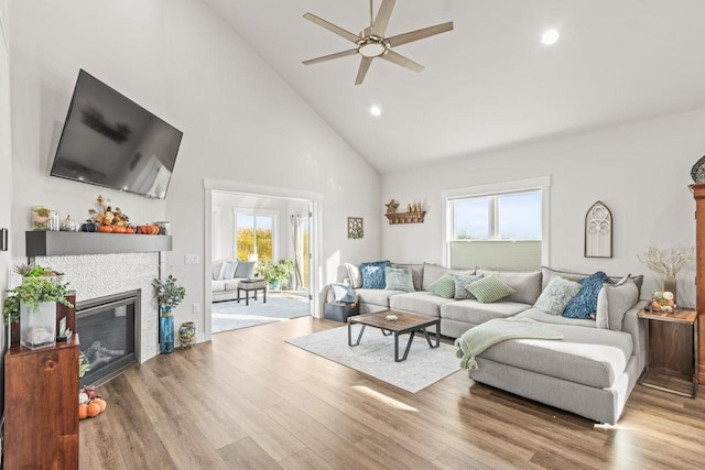 living room with light hardwood / wood-style floors, high vaulted ceiling, a fireplace, and ceiling fan