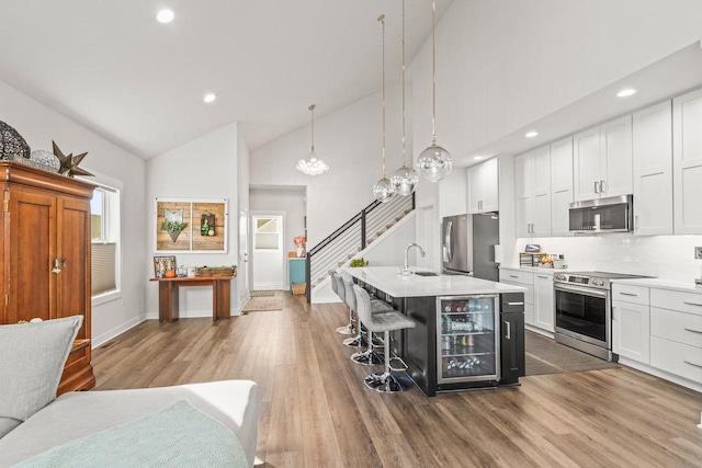 kitchen with beverage cooler, hanging light fixtures, a center island with sink, a kitchen breakfast bar, and stainless steel appliances