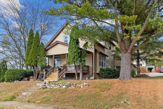 view of property hidden behind natural elements featuring a porch, a front yard, and a garage