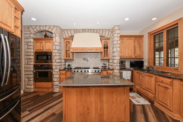 kitchen with a kitchen island, stainless steel appliances, dark stone countertops, premium range hood, and dark hardwood / wood-style flooring