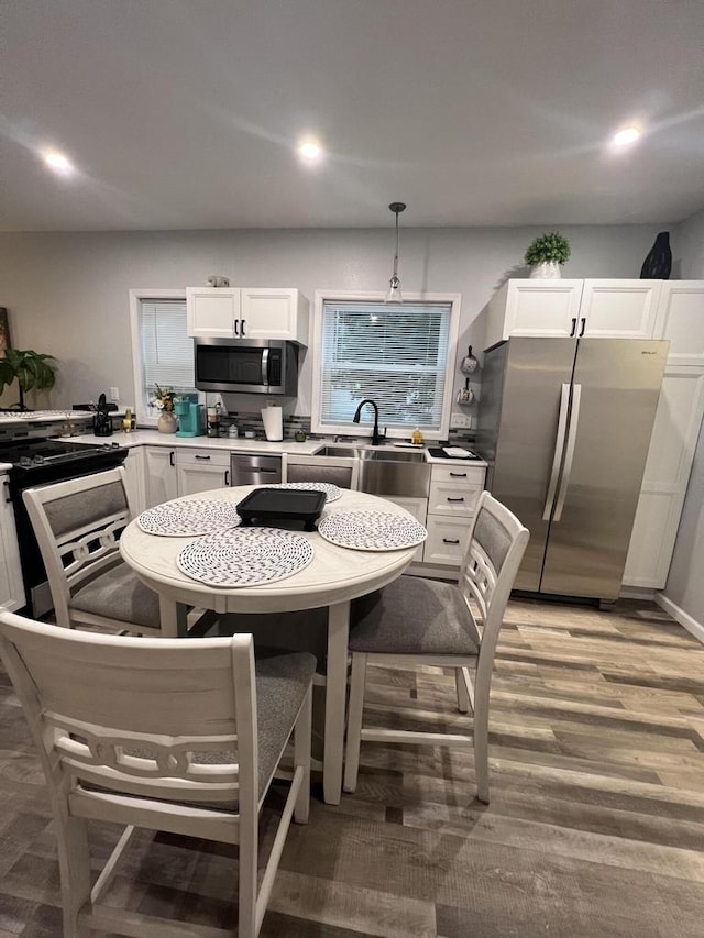 kitchen featuring white cabinetry, pendant lighting, appliances with stainless steel finishes, and light hardwood / wood-style flooring