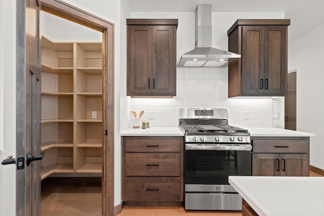 kitchen featuring wall chimney range hood, decorative backsplash, stainless steel range with gas stovetop, light hardwood / wood-style floors, and dark brown cabinetry