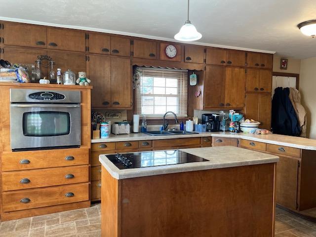 kitchen featuring decorative light fixtures, black electric stovetop, a kitchen island, sink, and stainless steel oven