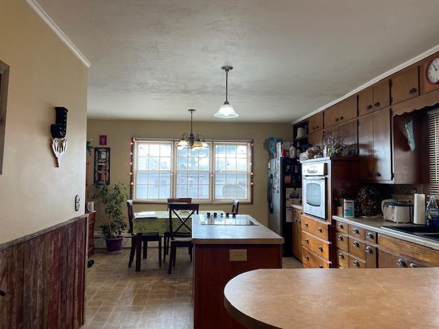 kitchen with oven, a center island, pendant lighting, ornamental molding, and a chandelier