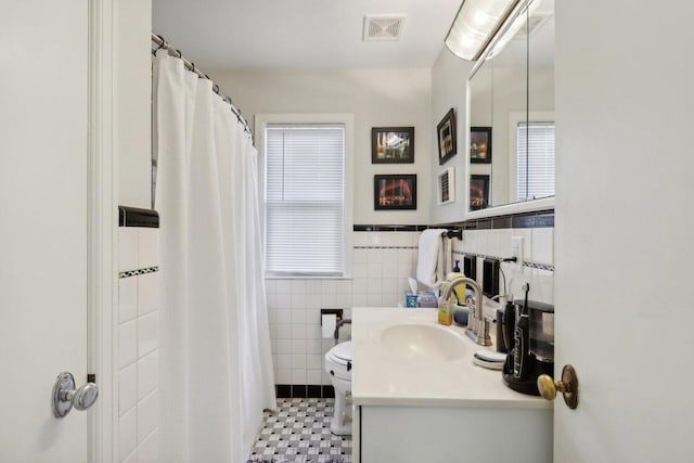 bathroom with tile patterned floors, toilet, vanity, tile walls, and walk in shower