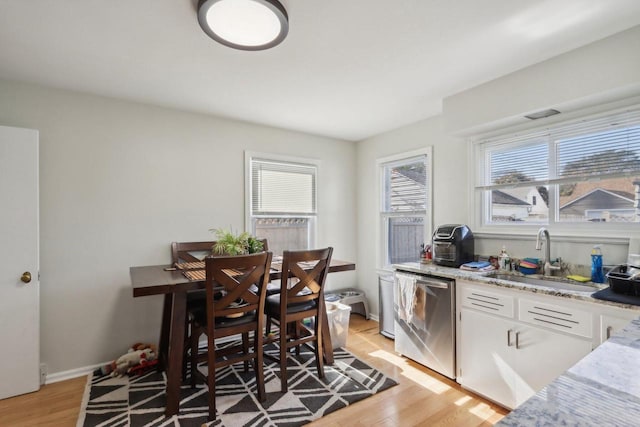 kitchen with sink, light stone countertops, stainless steel dishwasher, white cabinetry, and light hardwood / wood-style floors