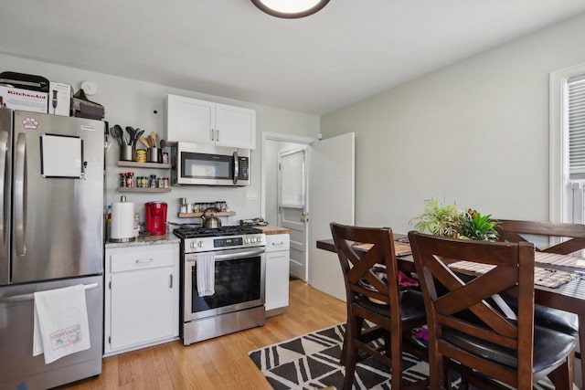 kitchen with appliances with stainless steel finishes, light wood-type flooring, and white cabinets