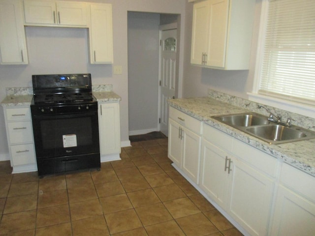 kitchen with white cabinets, light stone counters, black range with gas stovetop, dark tile patterned flooring, and sink