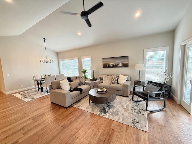 living room featuring ceiling fan with notable chandelier, plenty of natural light, light hardwood / wood-style floors, and vaulted ceiling