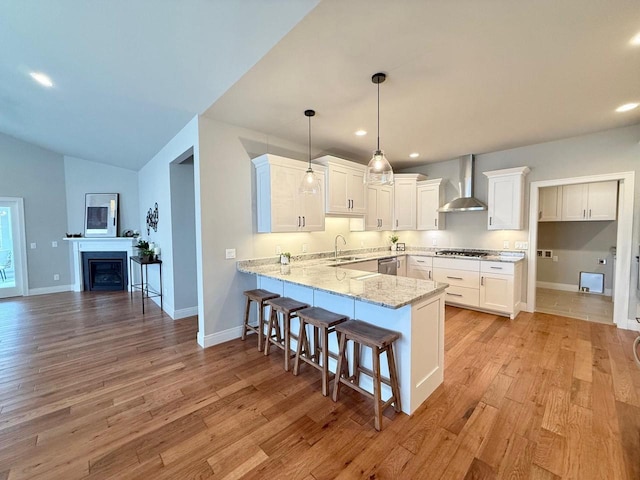 kitchen featuring sink, kitchen peninsula, wall chimney exhaust hood, decorative light fixtures, and white cabinets