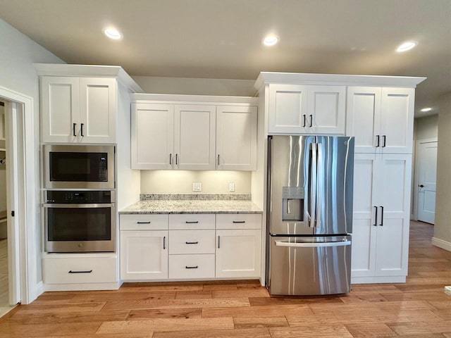 kitchen with light wood-type flooring, appliances with stainless steel finishes, light stone counters, and white cabinets