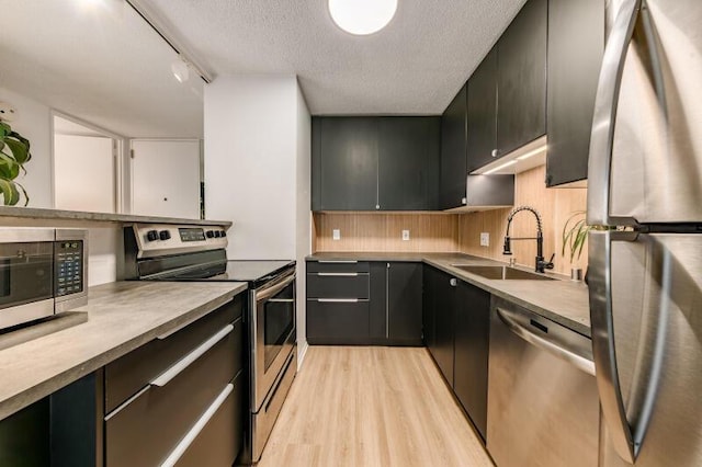 kitchen with light wood-type flooring, appliances with stainless steel finishes, a textured ceiling, track lighting, and sink