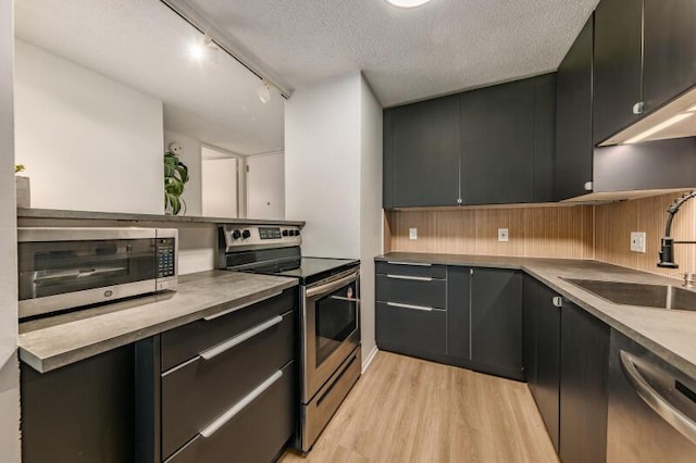 kitchen featuring appliances with stainless steel finishes, a textured ceiling, track lighting, sink, and light hardwood / wood-style flooring