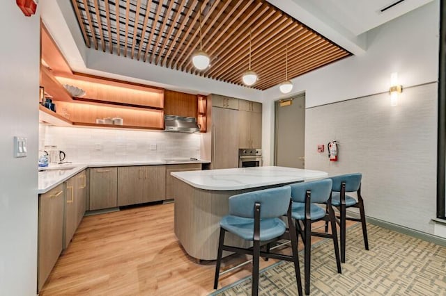 kitchen with oven, tasteful backsplash, a kitchen breakfast bar, ventilation hood, and light wood-type flooring